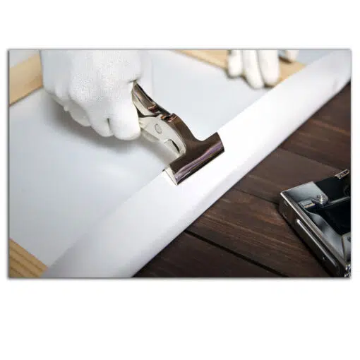 Close-up of a canvas being stretched over a wooden frame using pliers, with gloved hands.